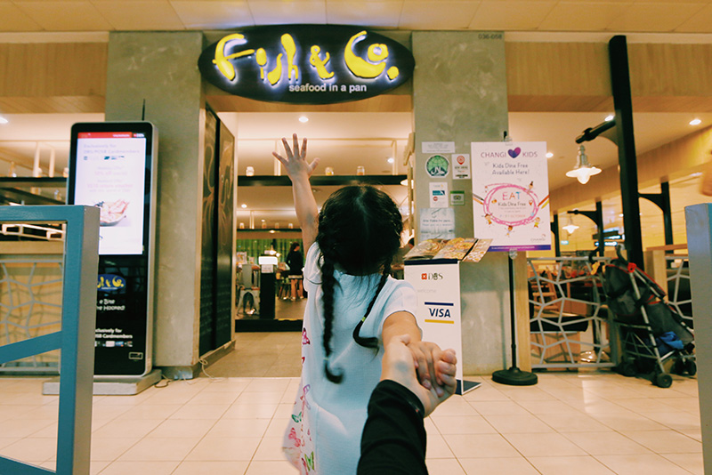 A young girl standing outside the Fish & Co outlet at Changi Airport